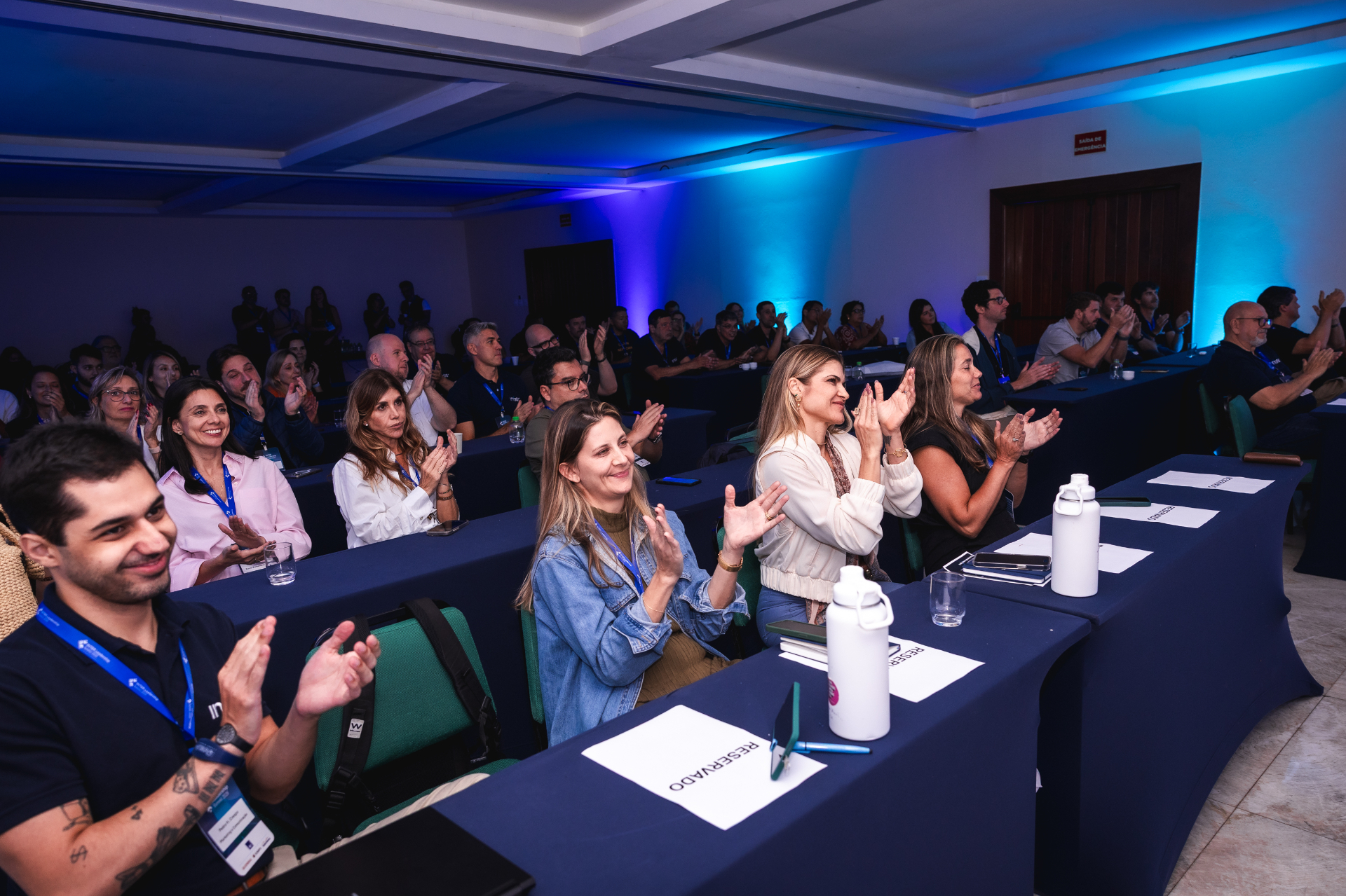 Plenária lotada com iluminação cênica azul durante apresentação