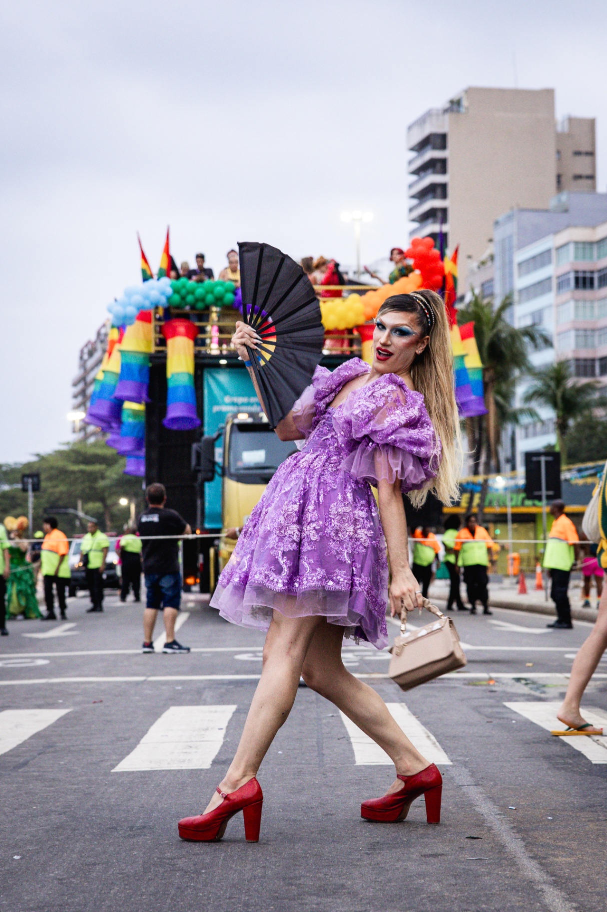 Drag queen com vestido lilás em frente a trio elétrico decorado com balões e bandeiras